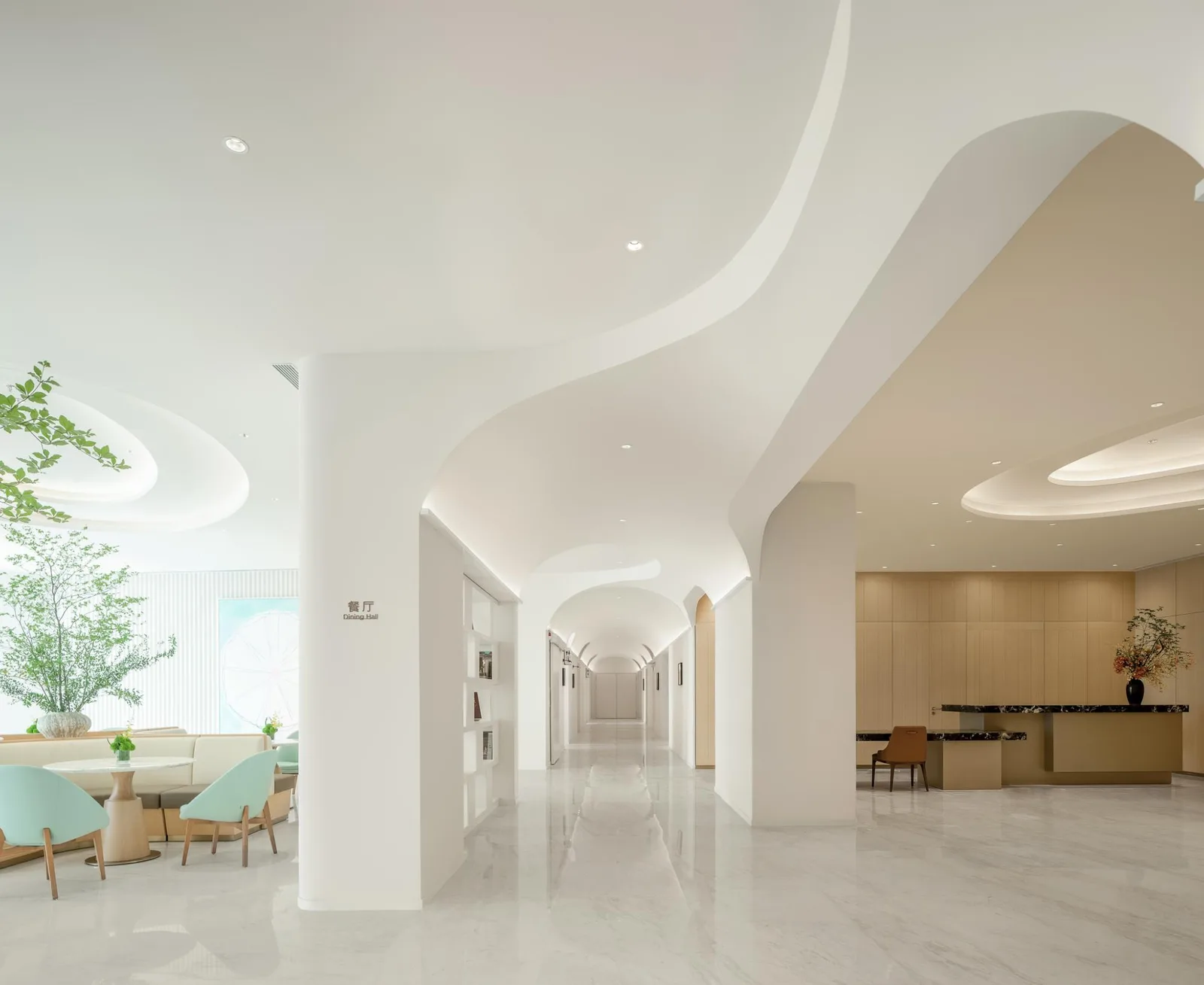 Bright modern interior hall of Shenzhen Qianhai Taikang Hospital with curved white architecture, greenery and reception area.
